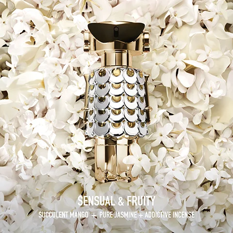 A gold perfume bottle with a scaled, metallic body stands on a bed of white flowers, with the text Sensual & Fruity, Succulent Mango + Pure Jasmine + Addictive Incense.